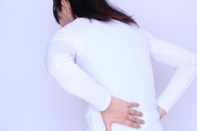 腰を押さえ辛そうな女性の画像