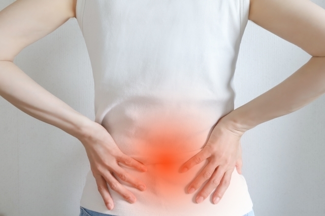 立った状態で腰を押さえている女性の後ろ姿の画像