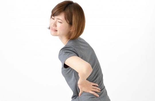 腰を押さえ辛そうにしている女性の左からの横顔