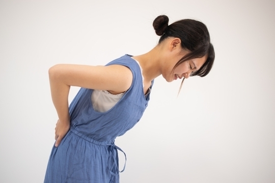 腰を押さえ辛そうにしている女性の右からの横顔