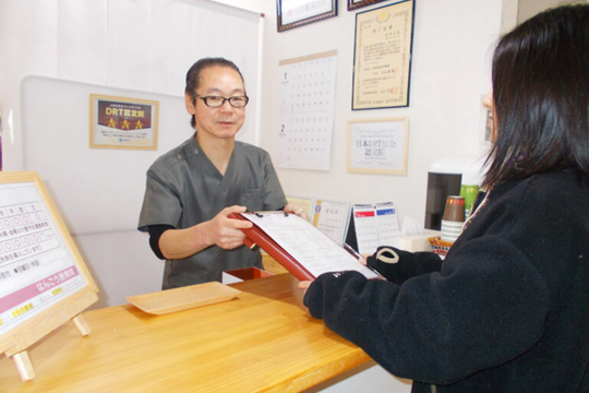 受付カウンターでバインダーを渡す院長とお客様